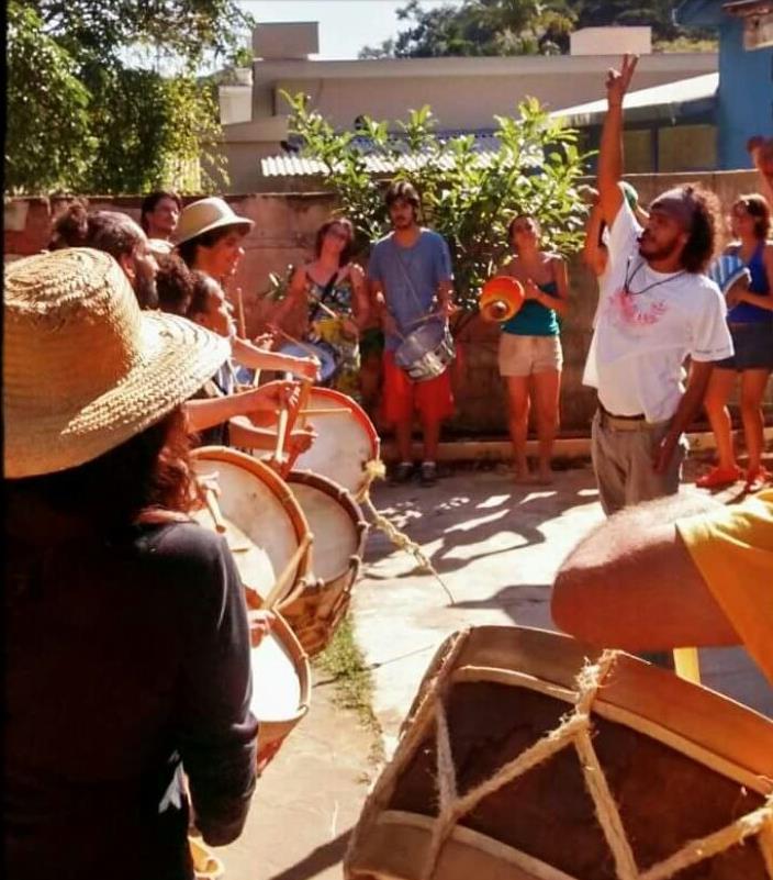 Roda de participantes tocando instrumentos de percussão ao ar livre na Casa da Paz.